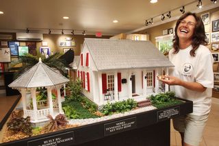 A woman smiling and laughing next to a diorama of a home.