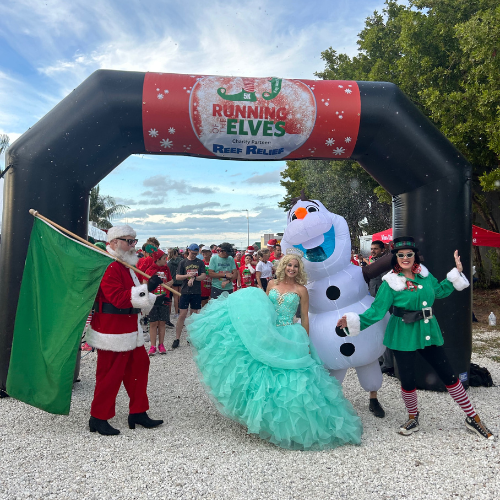 Santa, princess, snowman, and elf characters under a festive archway outdoors.