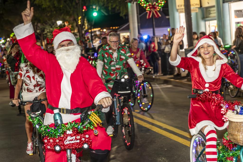 People in Christmas costumes riding festively decorated bikes at night.