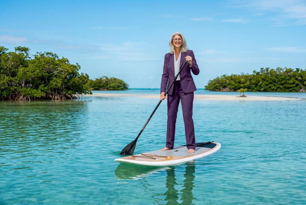 Woman in a purple suit paddleboarding on a calm, turquoise sea.