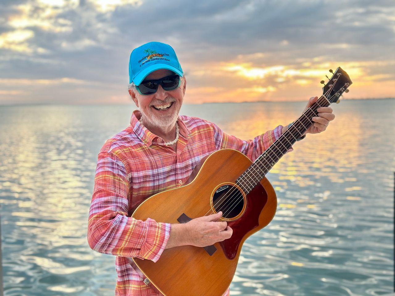 Man with guitar smiles by the sea at sunset.