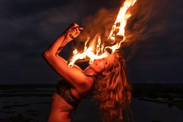 Fire performer holding a flaming torch near their mouth against a dark sky.