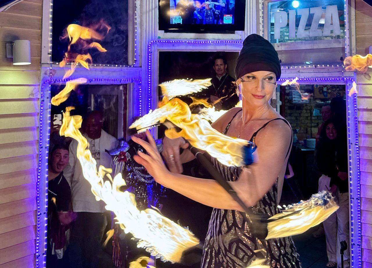 Performer twirling fire batons at night in front of a pizza shop.