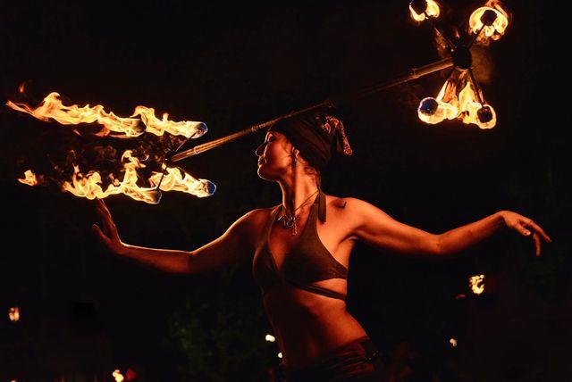 Fire dancer twirling flaming batons in a dark setting.