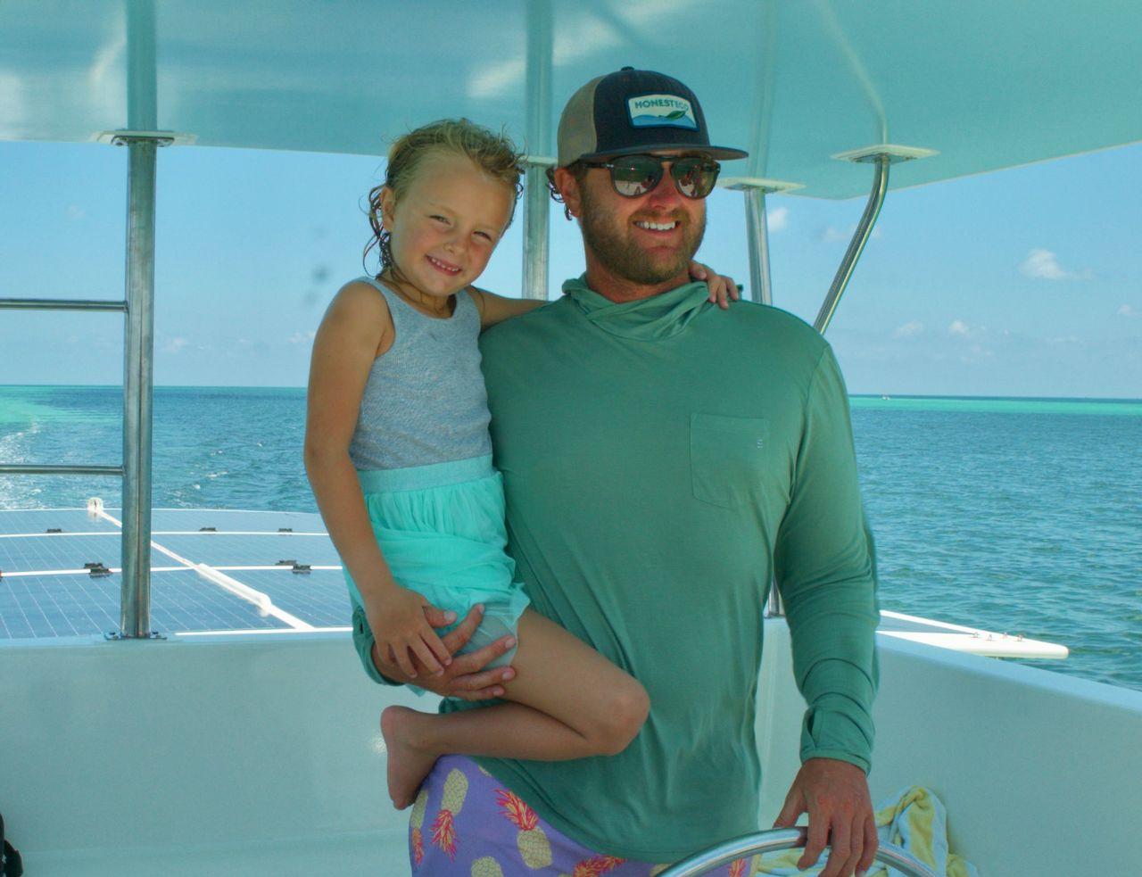 Man and child smiling on a boat with ocean view, sunny day.