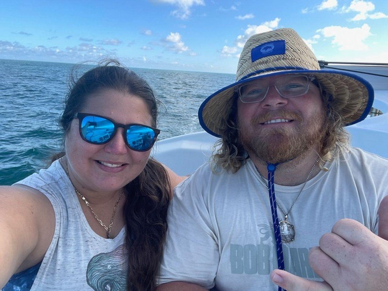 Smiling couple on a boat, sunny day, ocean in the background.