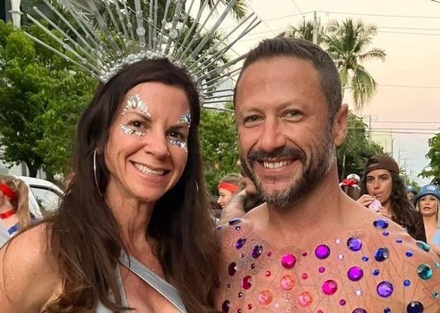 Two people smiling, wearing bright, decorative outfits at an outdoor event.