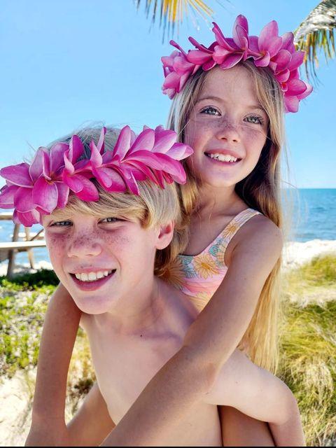 Kids with pink flower crowns, beach background, sunny day.