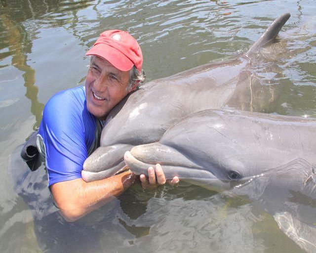 Man in water hugging two dolphins, smiling.