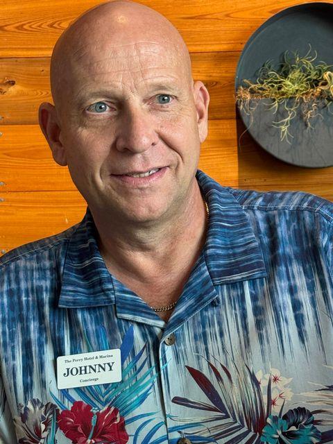 Bald man in a Hawaiian shirt smiling, wooden background.