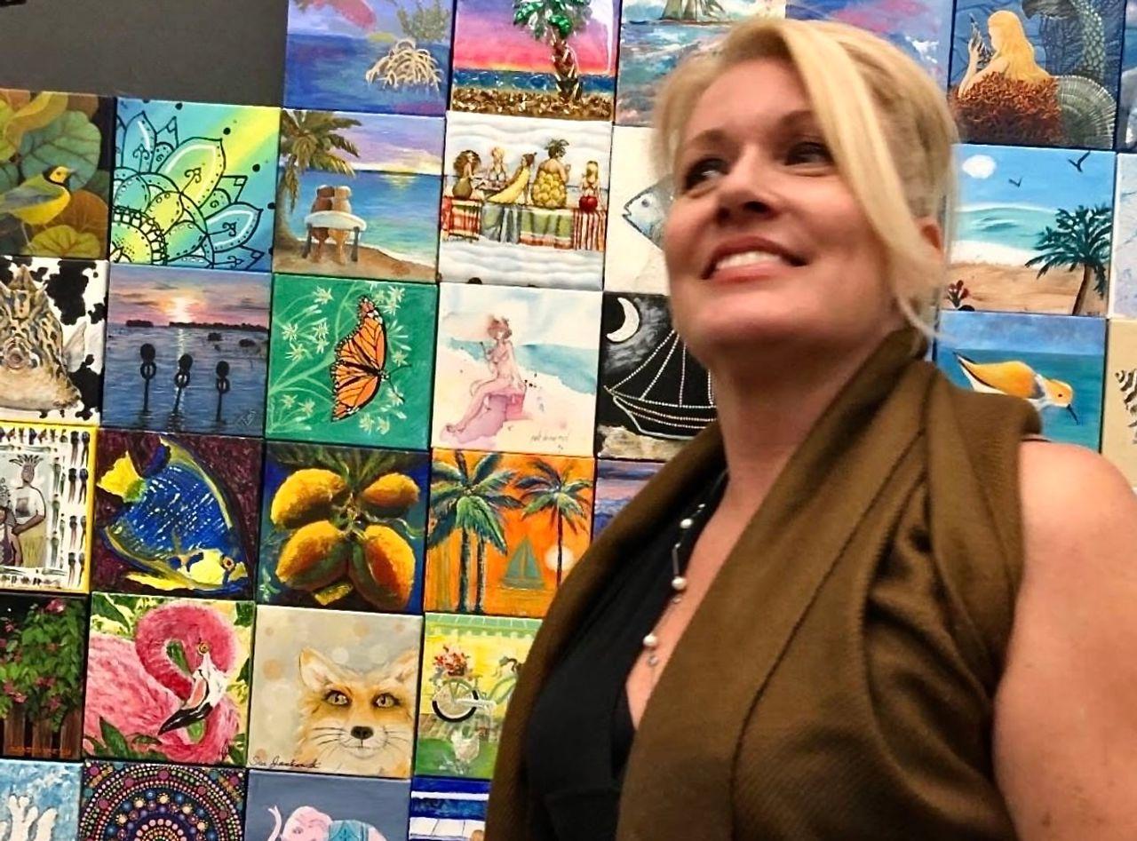 Woman smiling in front of a colorful wall of paintings.