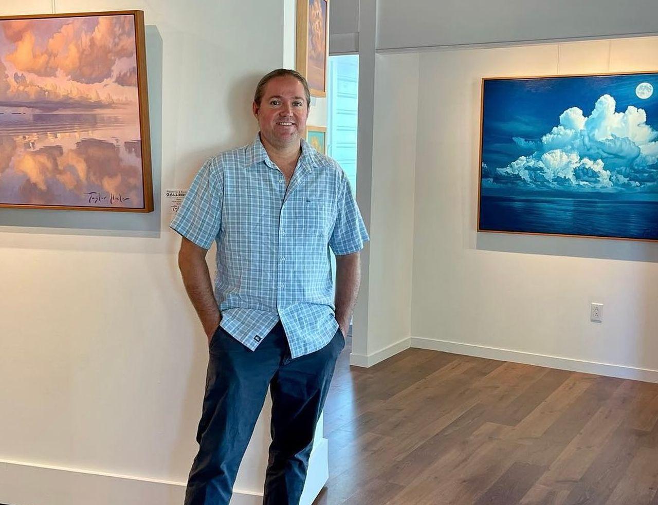 Man standing in art gallery, blue and pink paintings on the wall.
