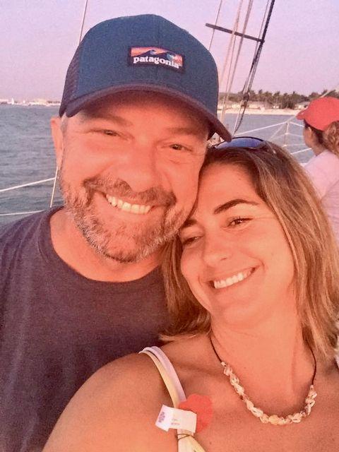 Couple smiling on a boat at sunset, ocean in background.