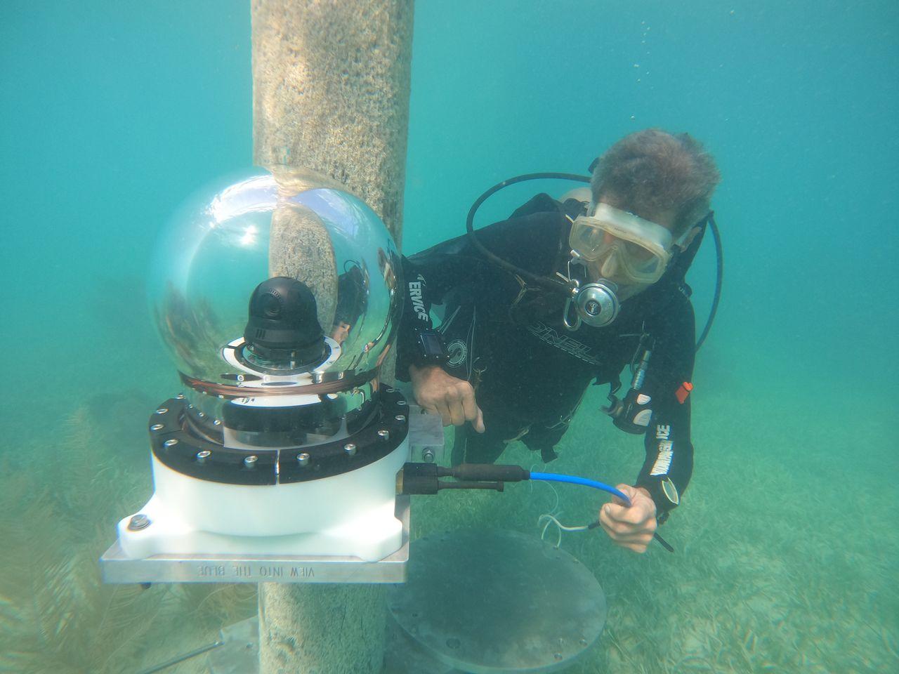 Scuba diver adjusts underwater camera on a pole.