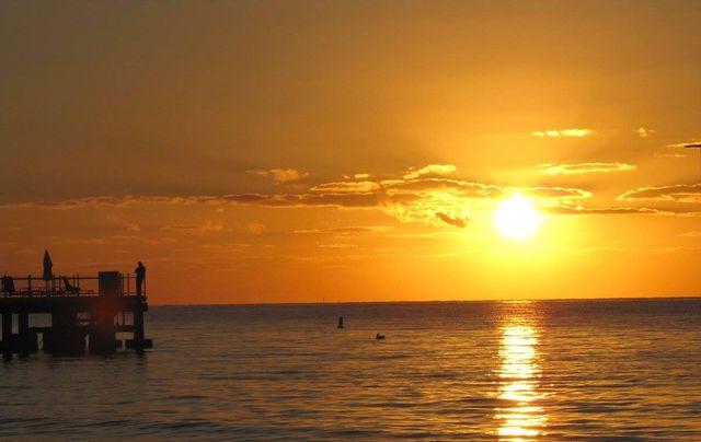 Sunset over the ocean with a pier silhouette on the left.