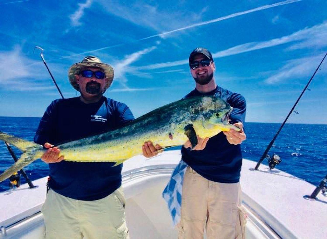 Two men on a boat holding a large fish under a clear blue sky.