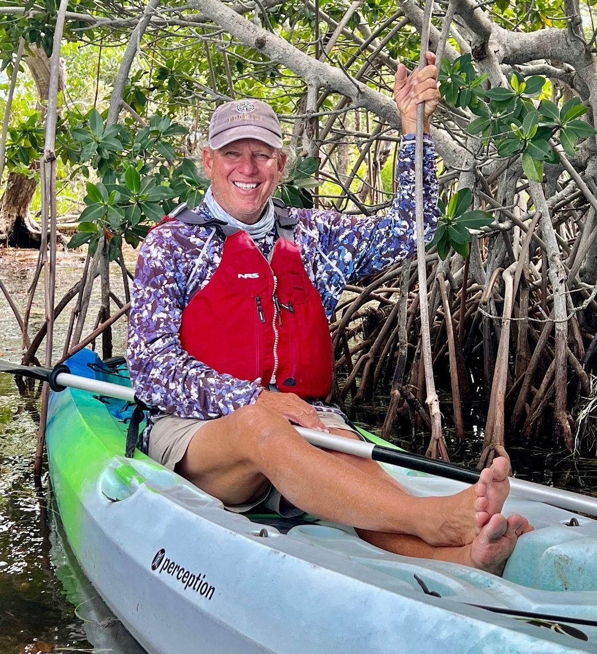 Man smiling in a kayak among mangrove trees.