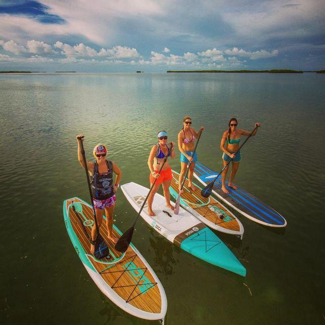 Four people paddleboarding on calm water under a cloudy sky.