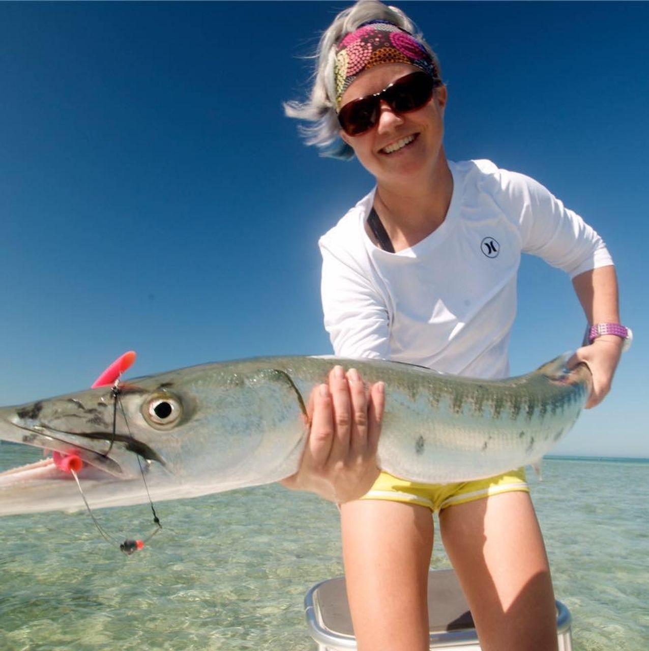 Smiling person holding a large fish on a sunny day by clear blue waters.