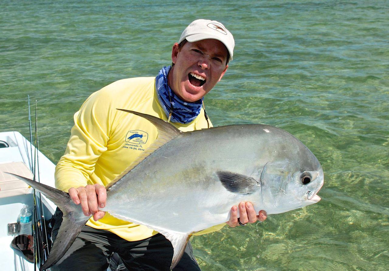 Man in yellow shirt excitedly holds large fish in clear water.