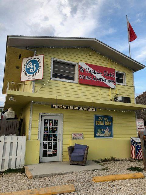 Two-story yellow building with signs, flags, and a chair outside. Cloudy sky.