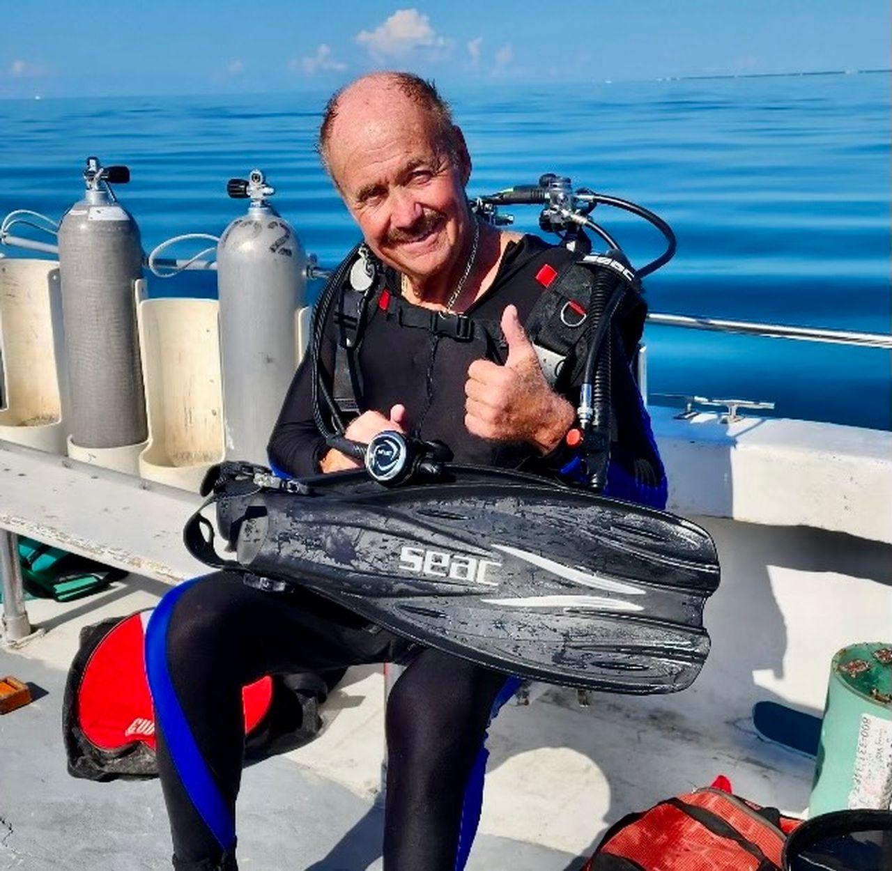 Scuba diver on a boat smiling and giving a thumbs-up.