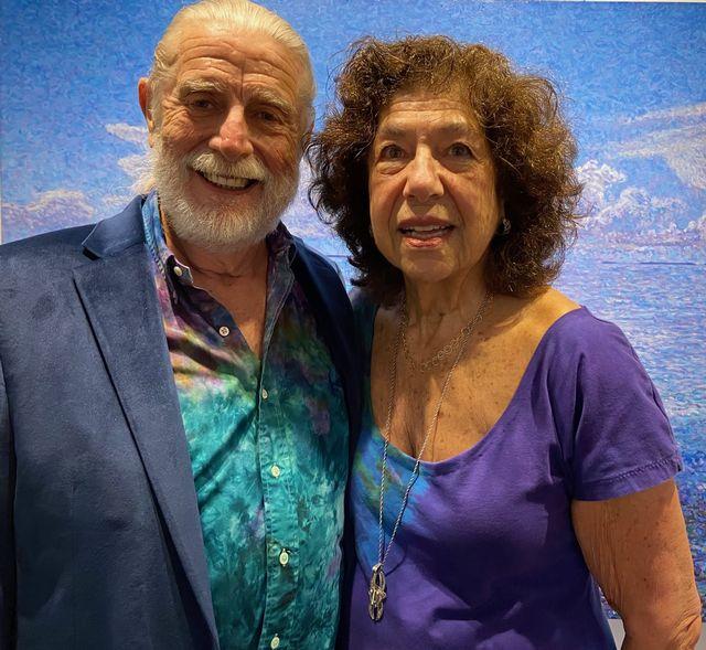 Elderly man and woman smiling, standing closely, with a blue ocean-themed backdrop.