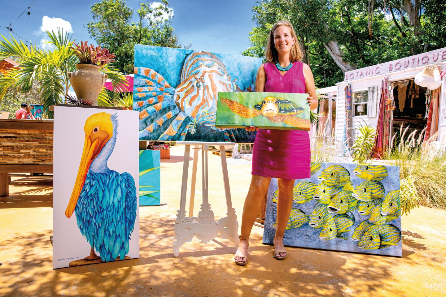 Woman in pink dress holding colorful paintings outdoors.
