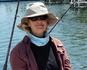 Person wearing a sun hat and sunglasses, fishing by a lake.