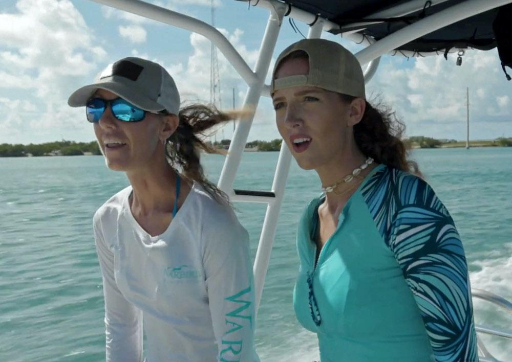 Two women on a boat, wearing hats and sun shirts, under a blue sky.