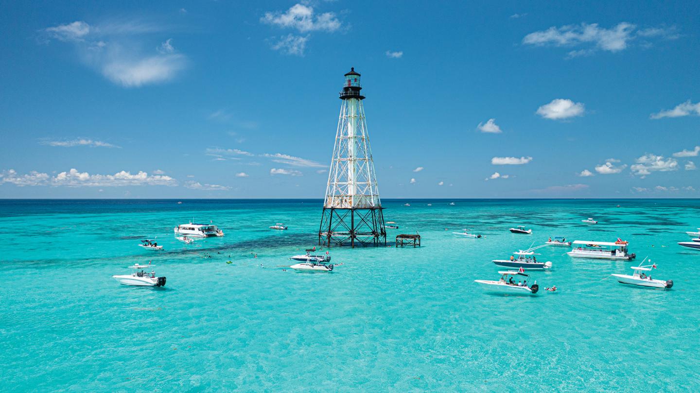 Clear blue sea with a lighthouse and boats under a sunny sky.