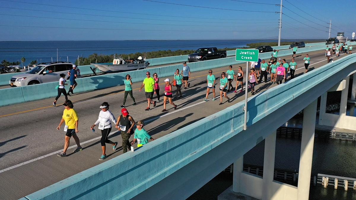 Runners on a coastal bridge during a sunny day marathon.