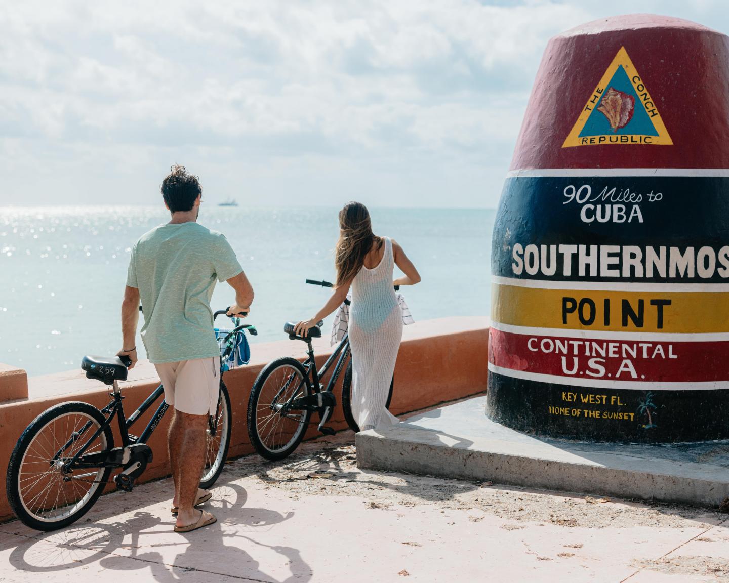 Couple with bicycles at a colorful landmark by the sea.