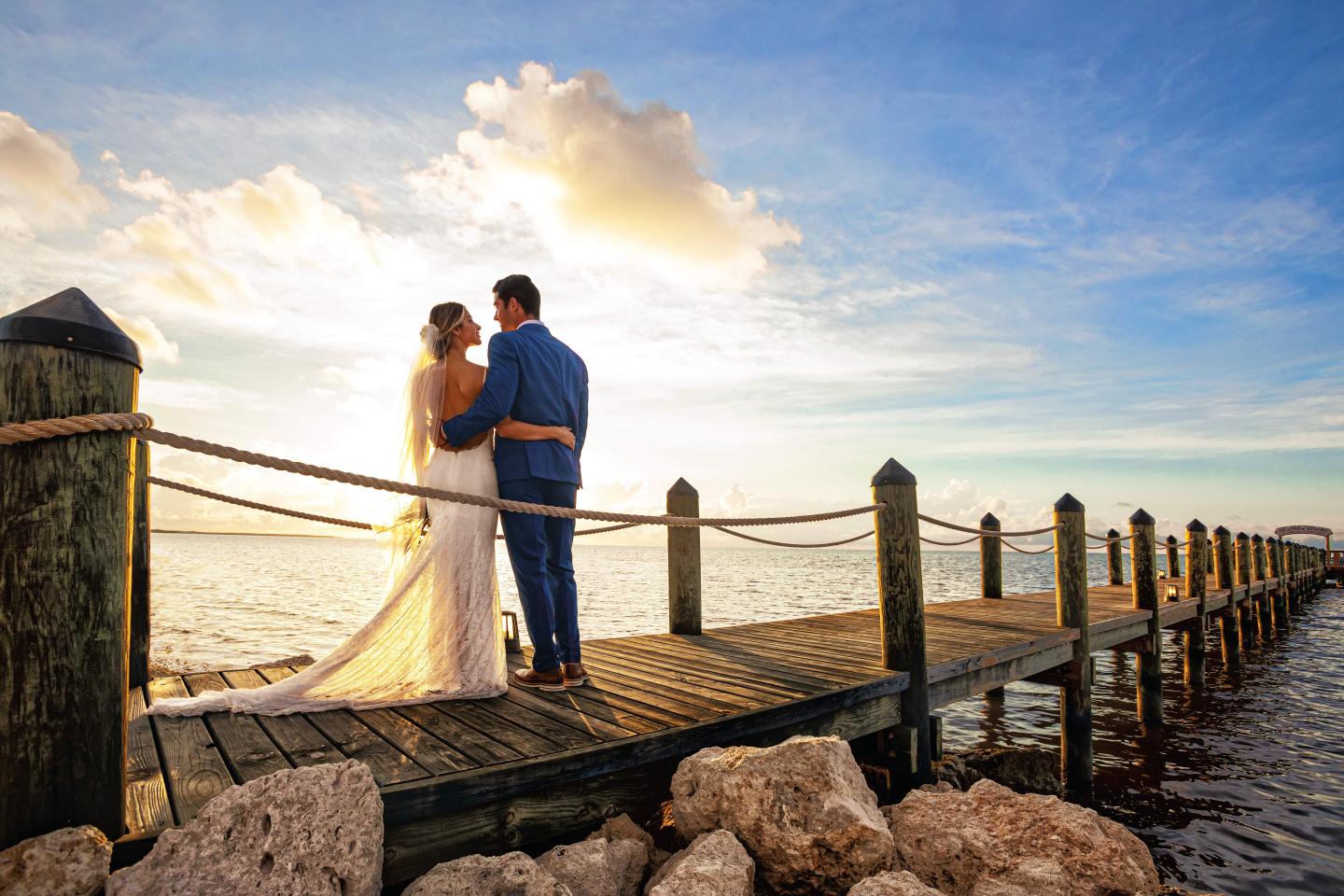 Bride and groom embrace on a pier at sunset.
