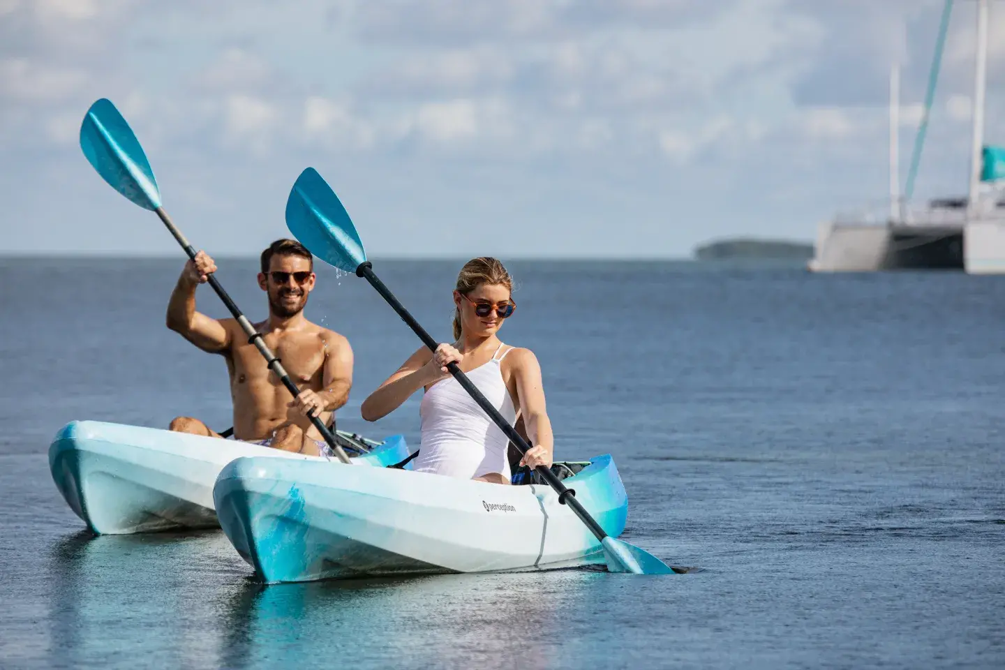 Two people kayaking together in a calm sea, with a boat in the distance.