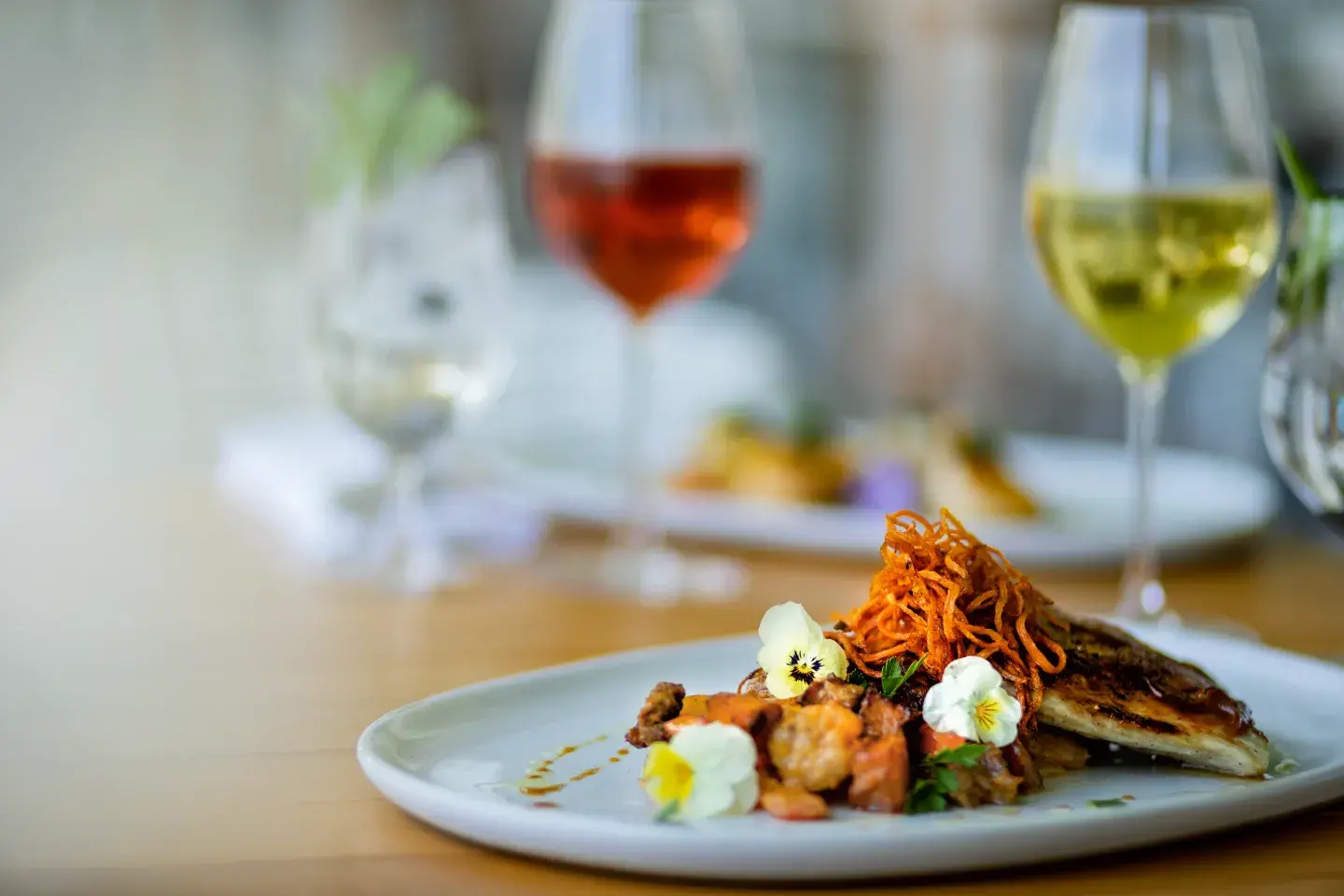 Gourmet dish with garnish, two glasses of wine in background.