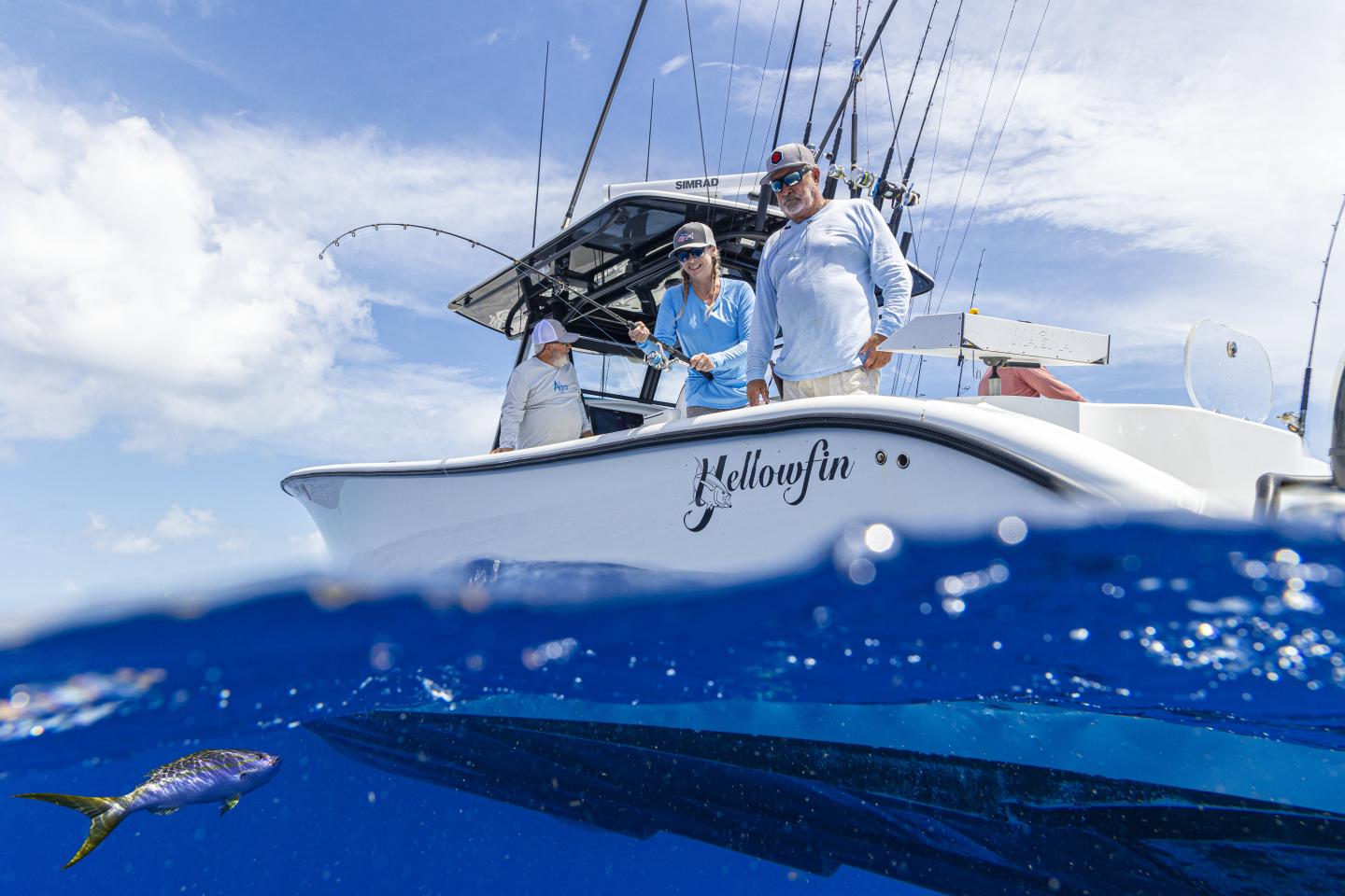 Boat with people fishing, blue ocean, small fish swimming nearby.