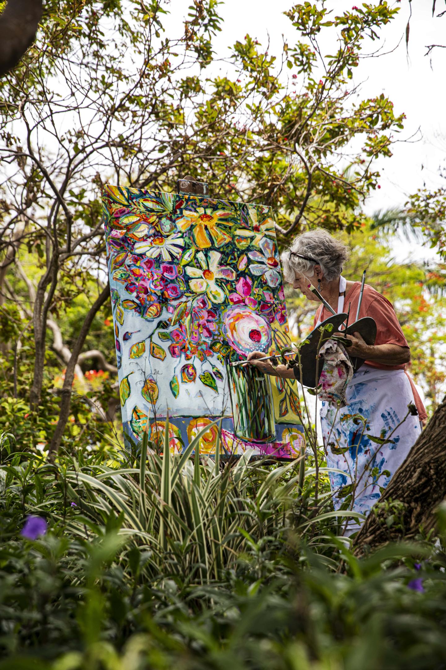 Artist painting colorful floral artwork in a lush garden setting.