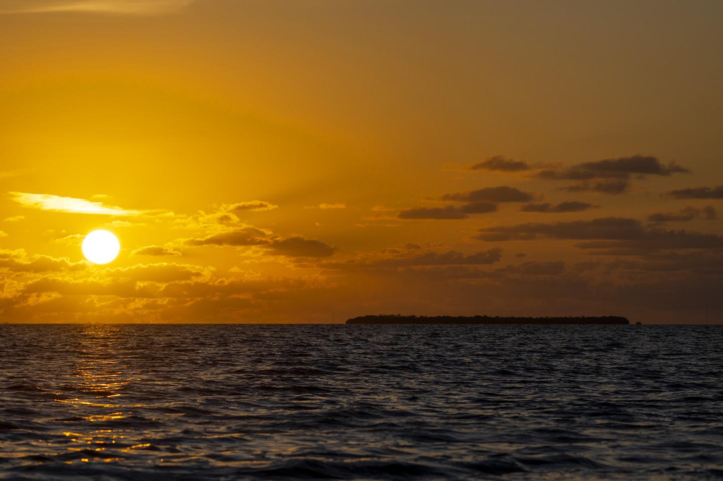 Sunset over the ocean, with an island silhouette and golden sky.