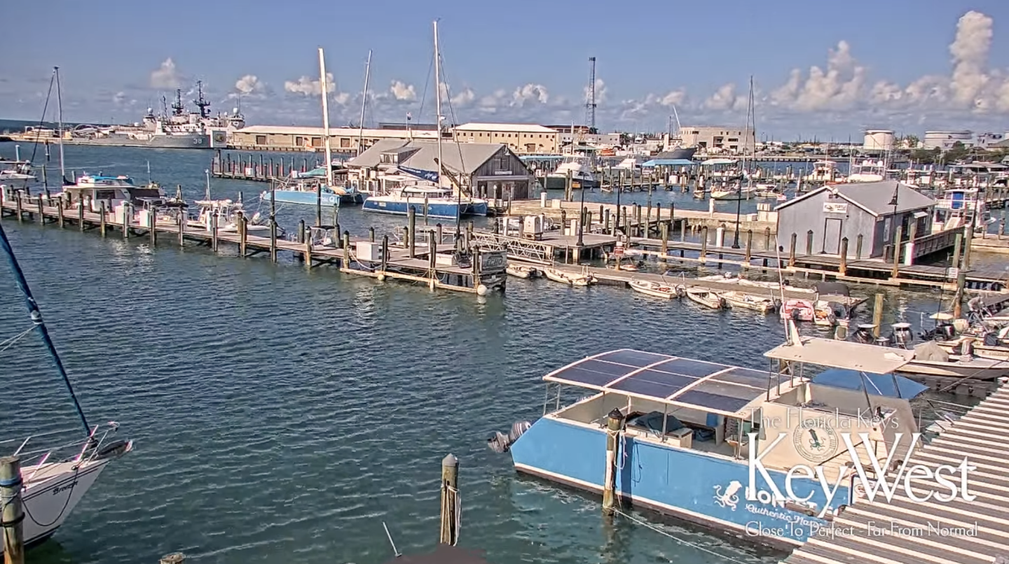 Marina with boats docked, clear sky, and distant warehouses.