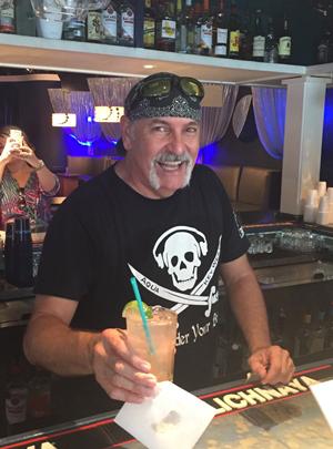 Man with a bandana and skull shirt smiling behind a bar.