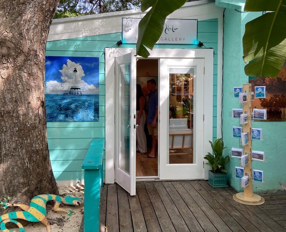 Turquoise art gallery exterior with open door under tree shade.