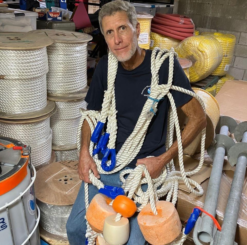 Man with ropes and buoys sitting in a warehouse.