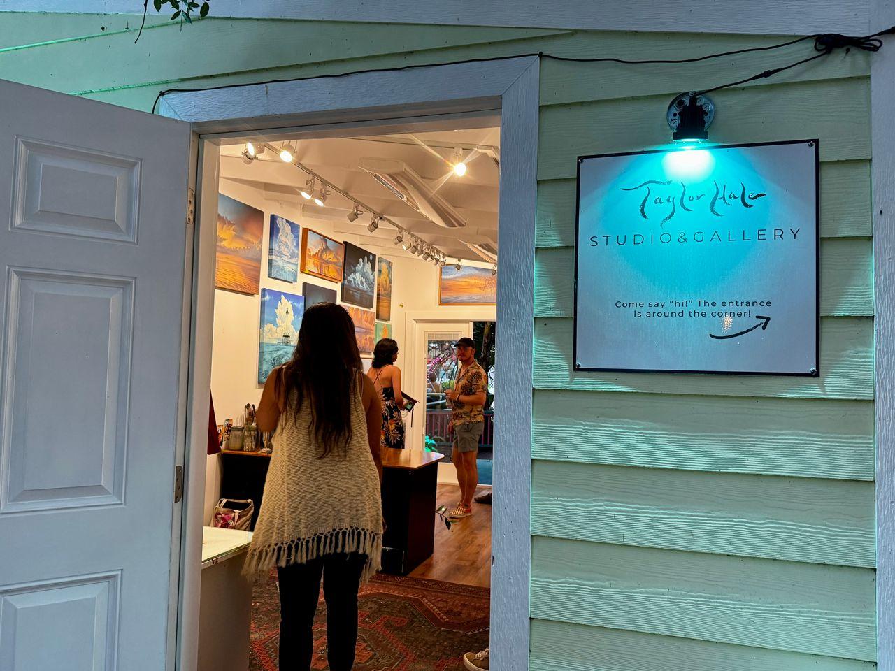 Open door to an art gallery, people inside viewing colorful paintings.