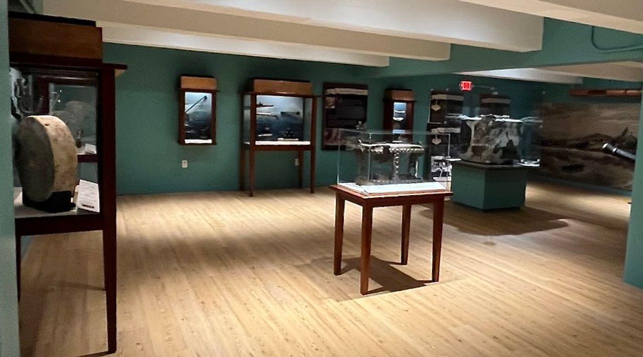 Museum exhibition room with glass display cases and artifacts on wooden flooring.