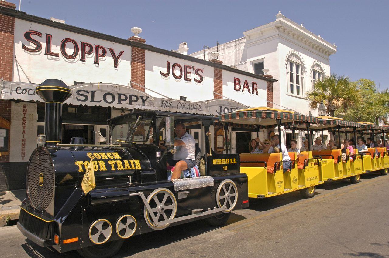 Black and yellow train in front of Sloppy Joe's Bar on a sunny street.