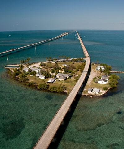 Small island with houses, connected by a long bridge over blue sea.