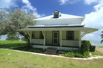 White house with a porch, surrounded by greenery under a blue sky.