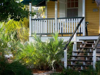 Yellow house with porch, greenery, and wooden steps.
