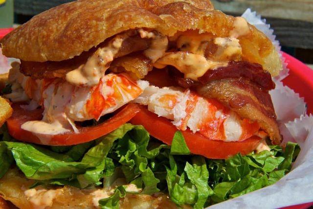 Lobster and bacon sandwich with lettuce and tomato on a red plate.